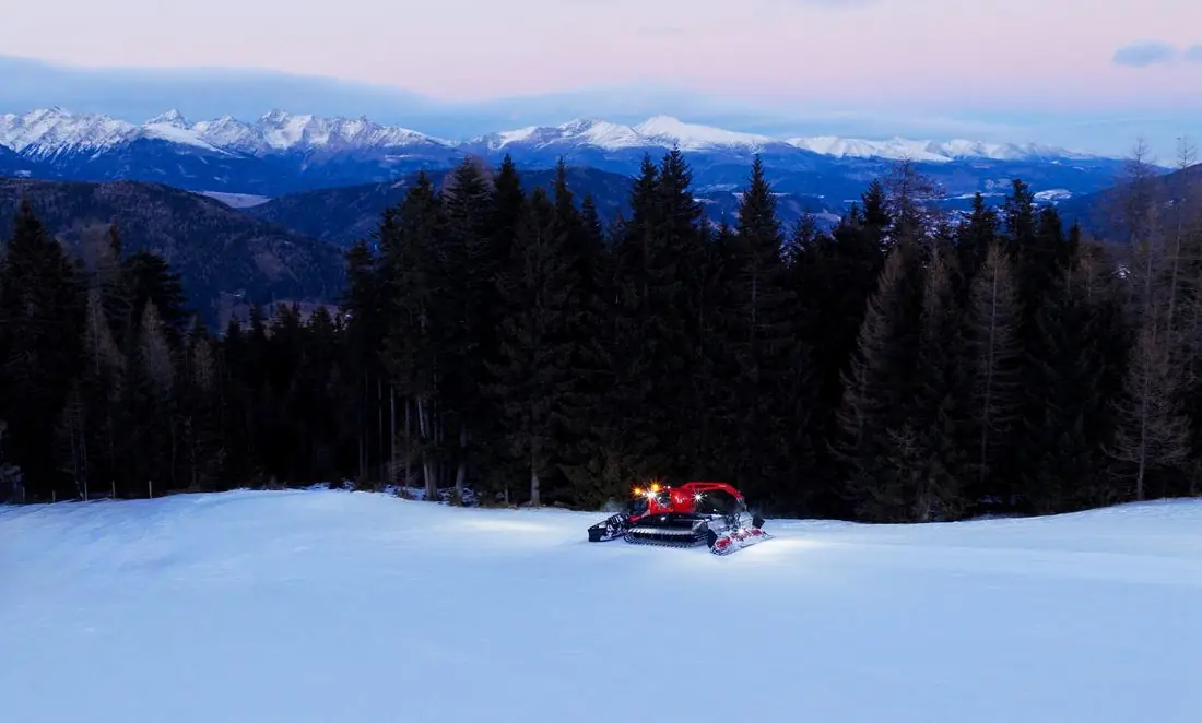 Pistenraupe mit Licht auf weiter Piste am Katschberg in der Abenddämmerung
