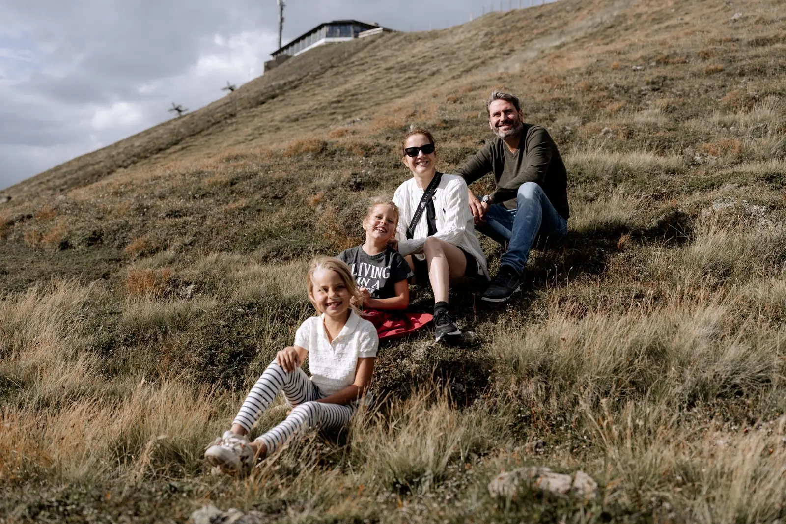 Familie sitzt auf der Almwiese am Aineck, oben die Bergstation