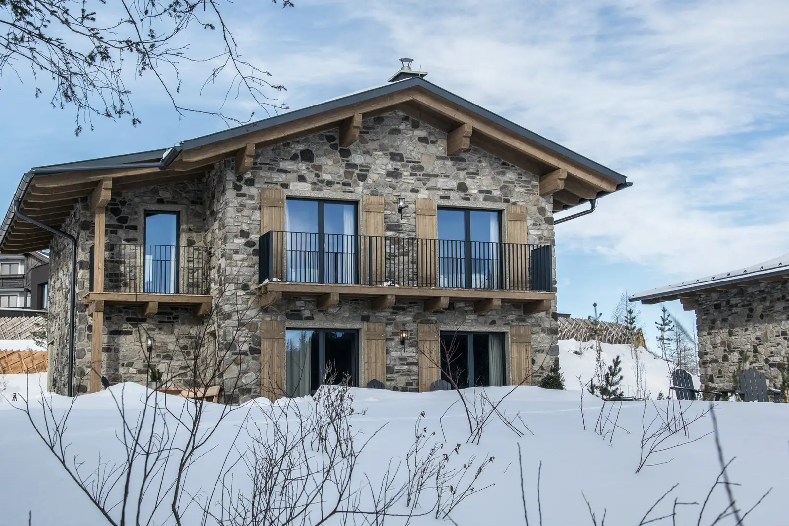Kauz Design Chalet mit Steinfassade und Holzbalkon im Schnee
