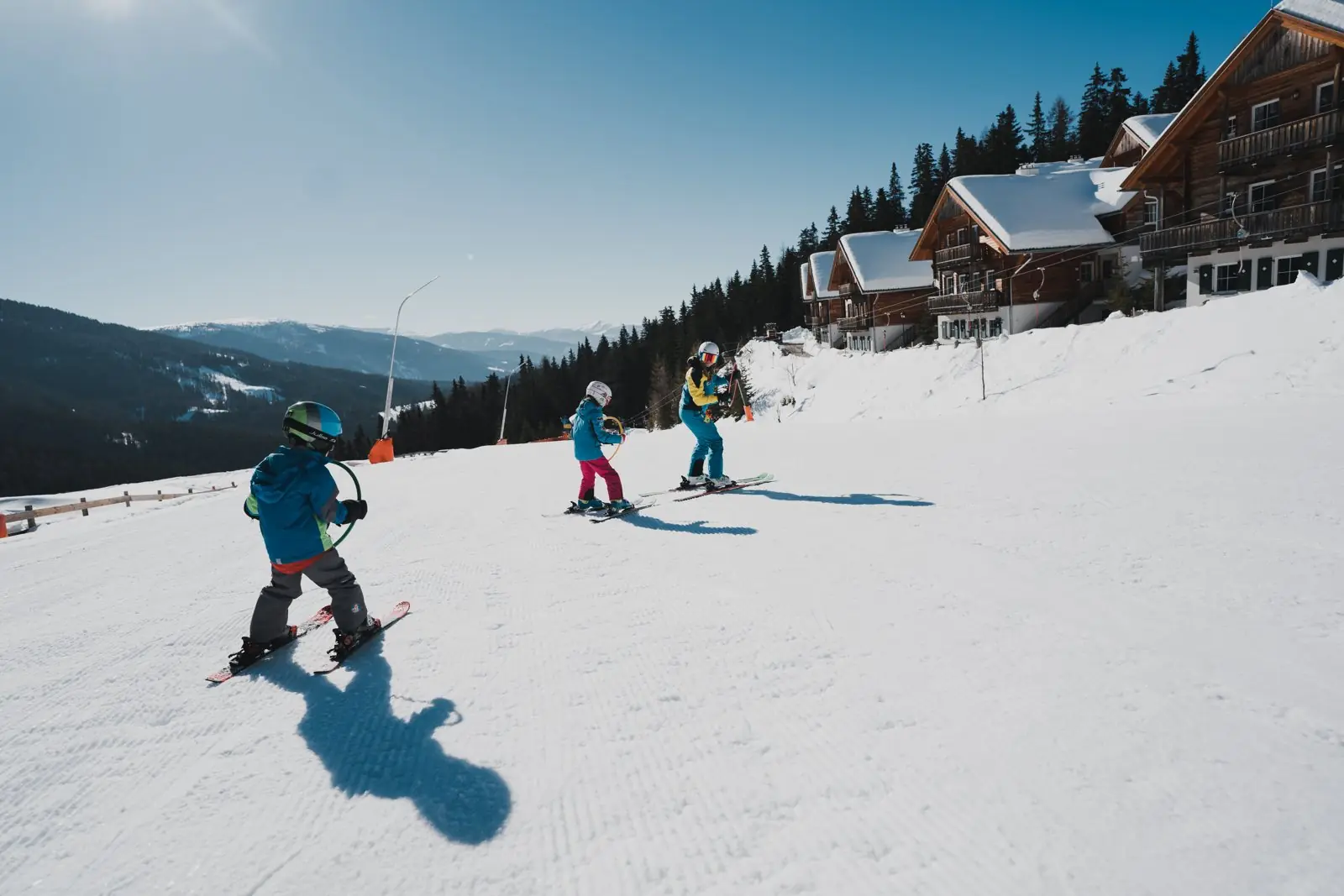 Kinder fahren im Skikurs mit Reifen hinter der Skilehrerin über das Übungsgelände am Katschberg