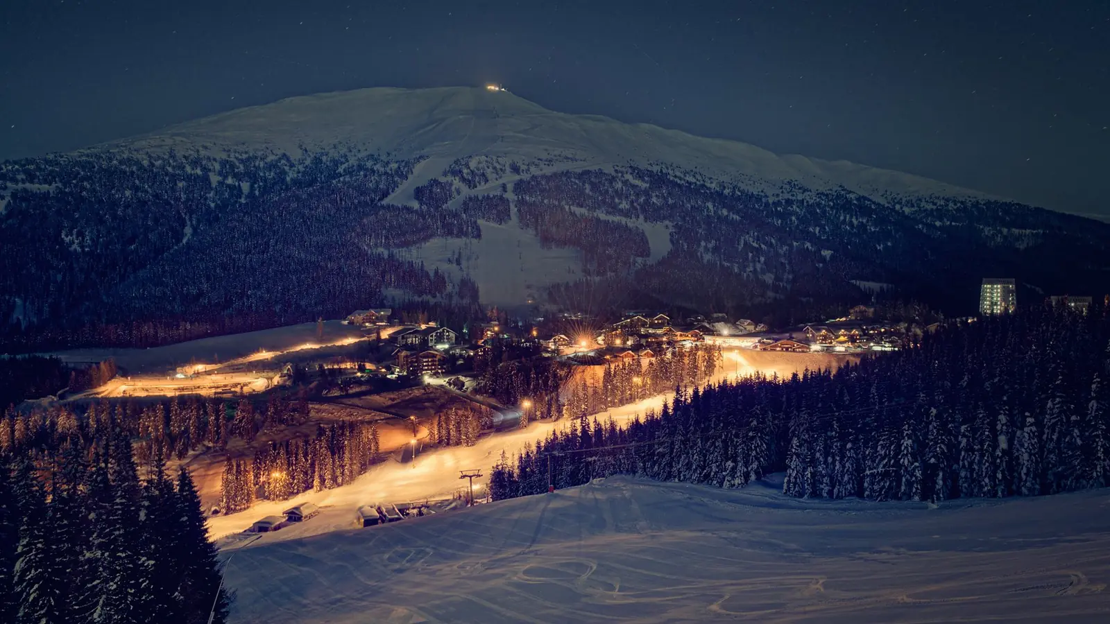 Beleuchtete Königswiese beim Nachtskilauf am Katschberg, darüber das verschneite Tschaneck unter dem Sternenhimmel