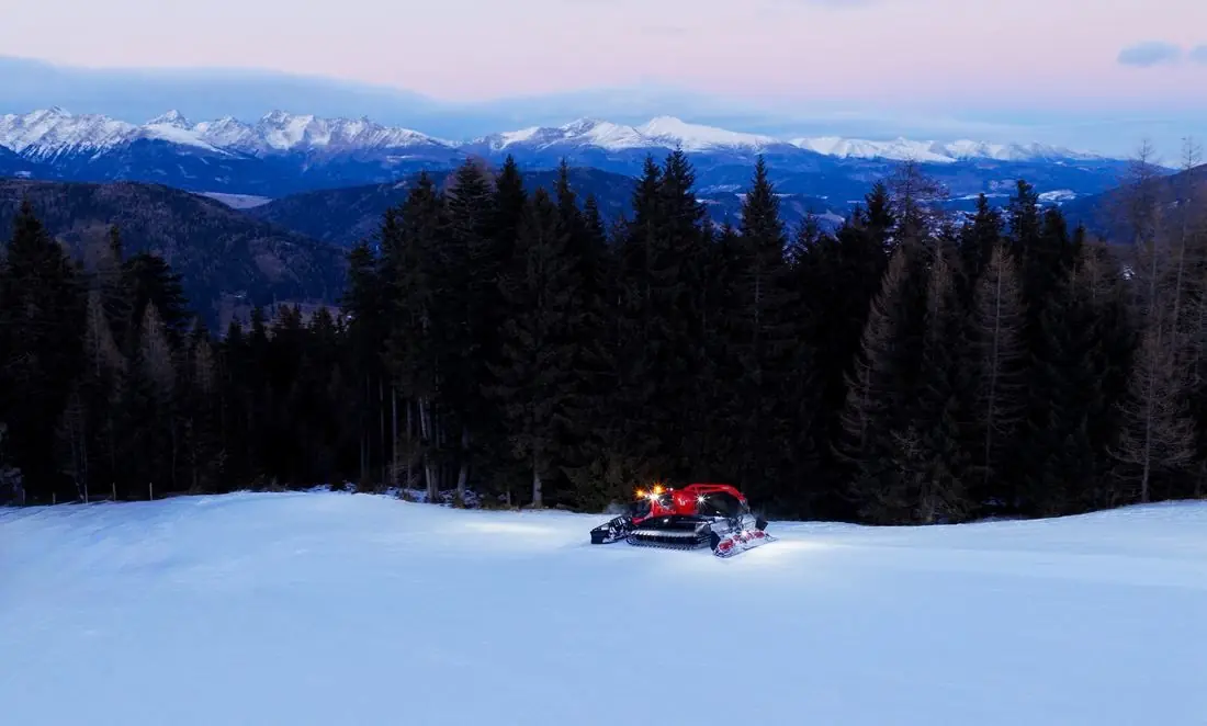 Pistenraupe mit Licht auf weiter Piste am Katschberg in der Abenddämmerung
